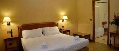 A hotel room with a large bed, two bedside tables, a nightstand, a mirror, and a wooden floor.