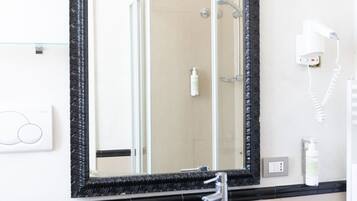 A bathroom with a black sink, a large mirror, a hairdryer, and a glass shower enclosure.