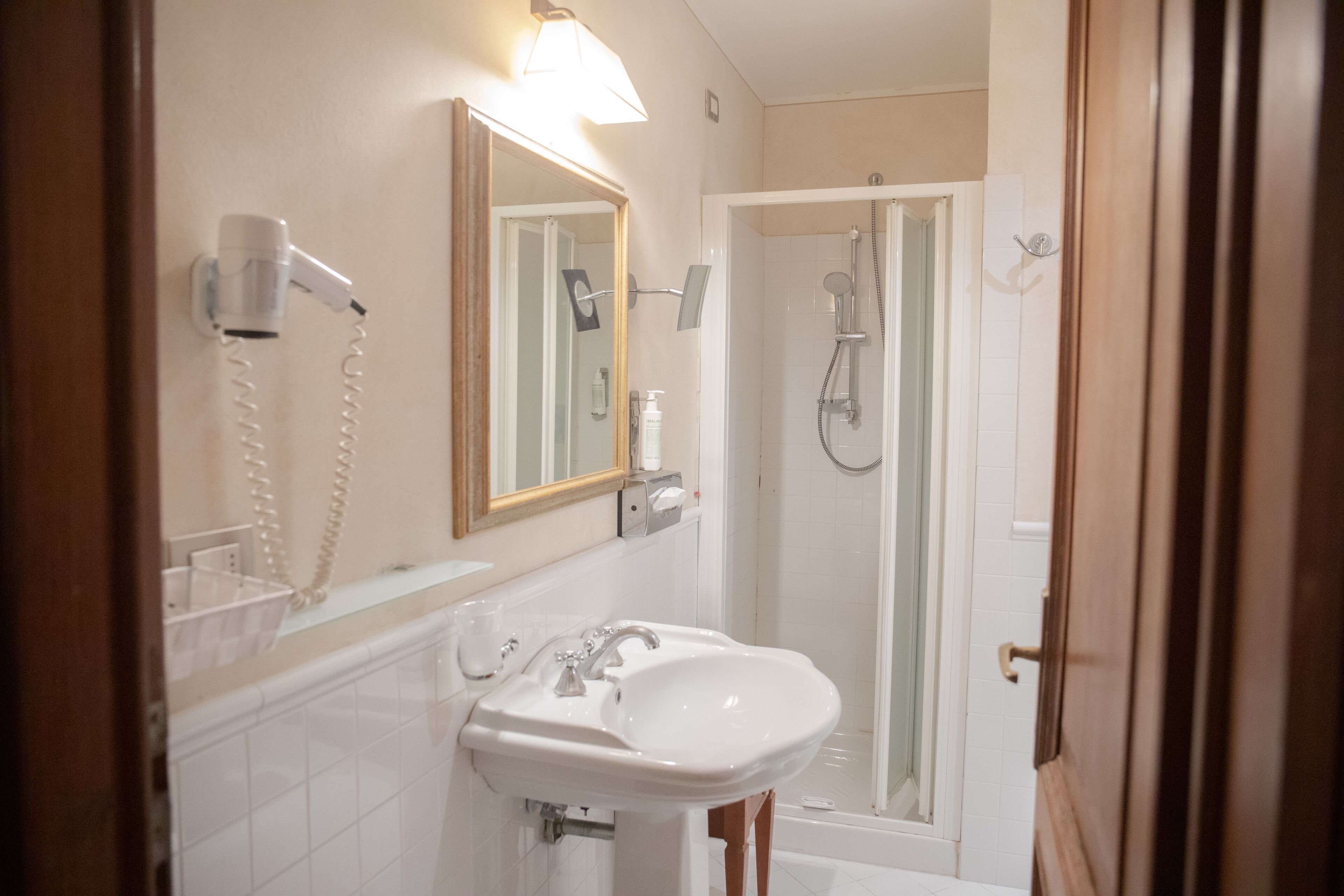 A bathroom with a white sink, a mirror, a hairdryer, and a shower.