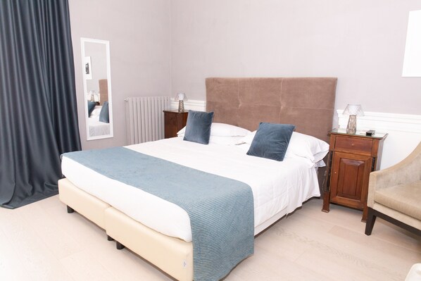 Un dormitorio ordenado con una cama grande, dos mesitas de noche, una silla y un espejo.