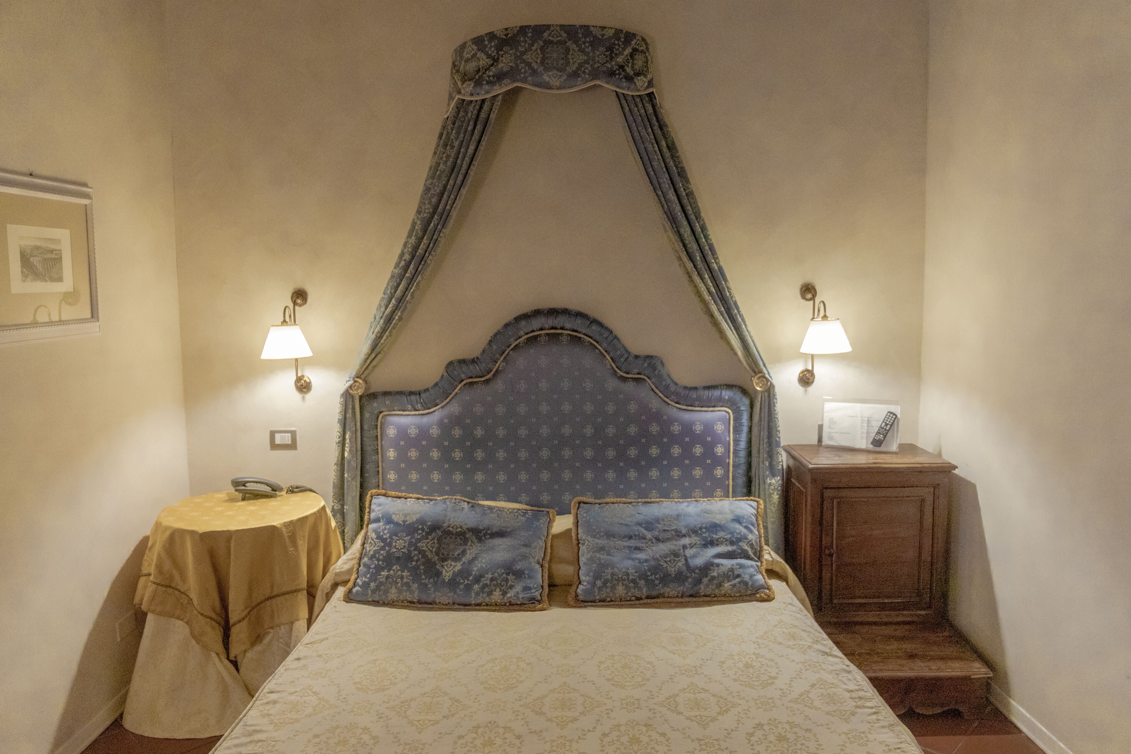 Une chambre à coucher avec un lit à baldaquin, deux lampes de chevet, une table de chevet avec une télécommande et une petite table avec une lampe.