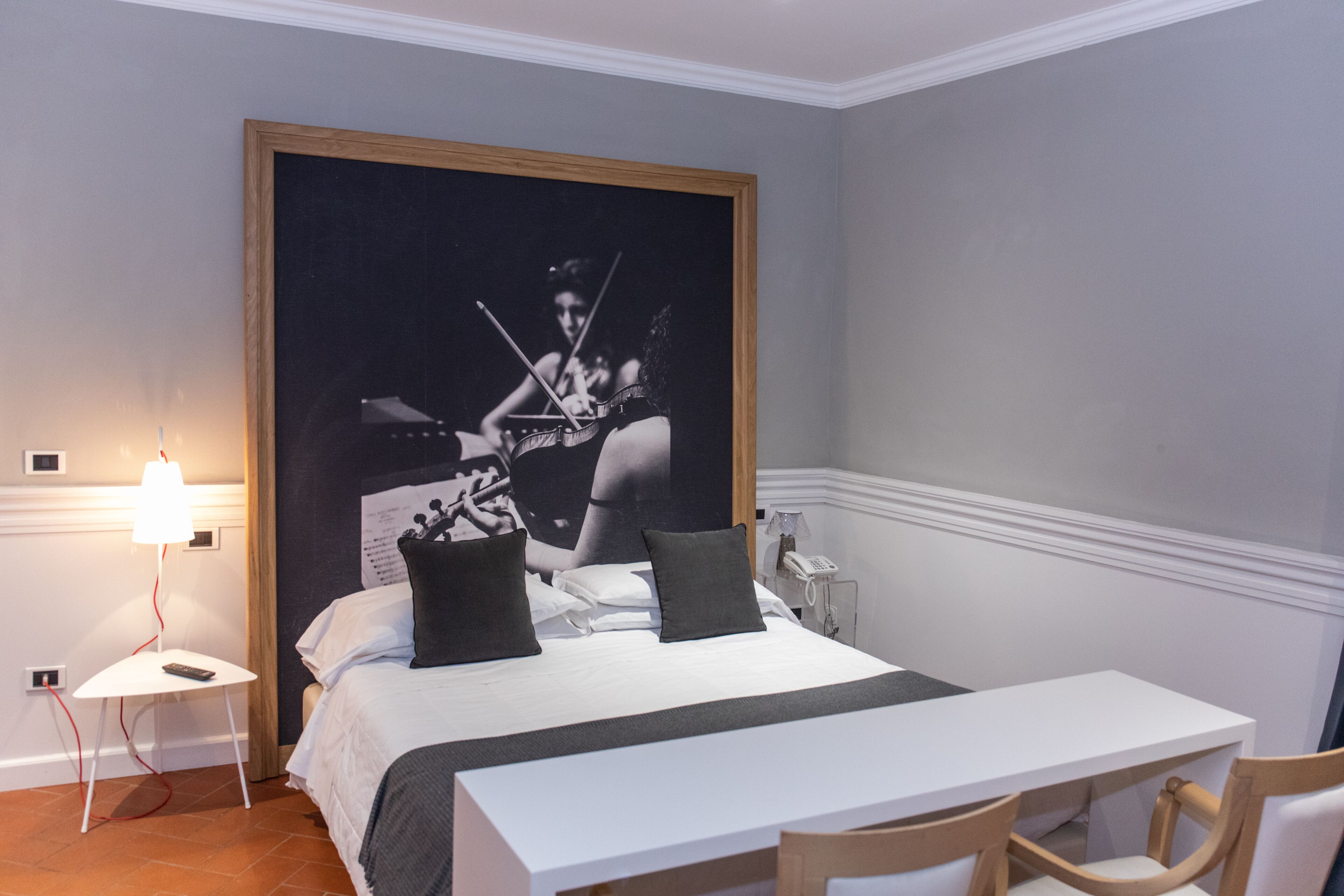 Ein Schlafzimmer mit einem Bett, einem Nachttisch, einer Lampe und einem großen gerahmten Bild an der Wand.