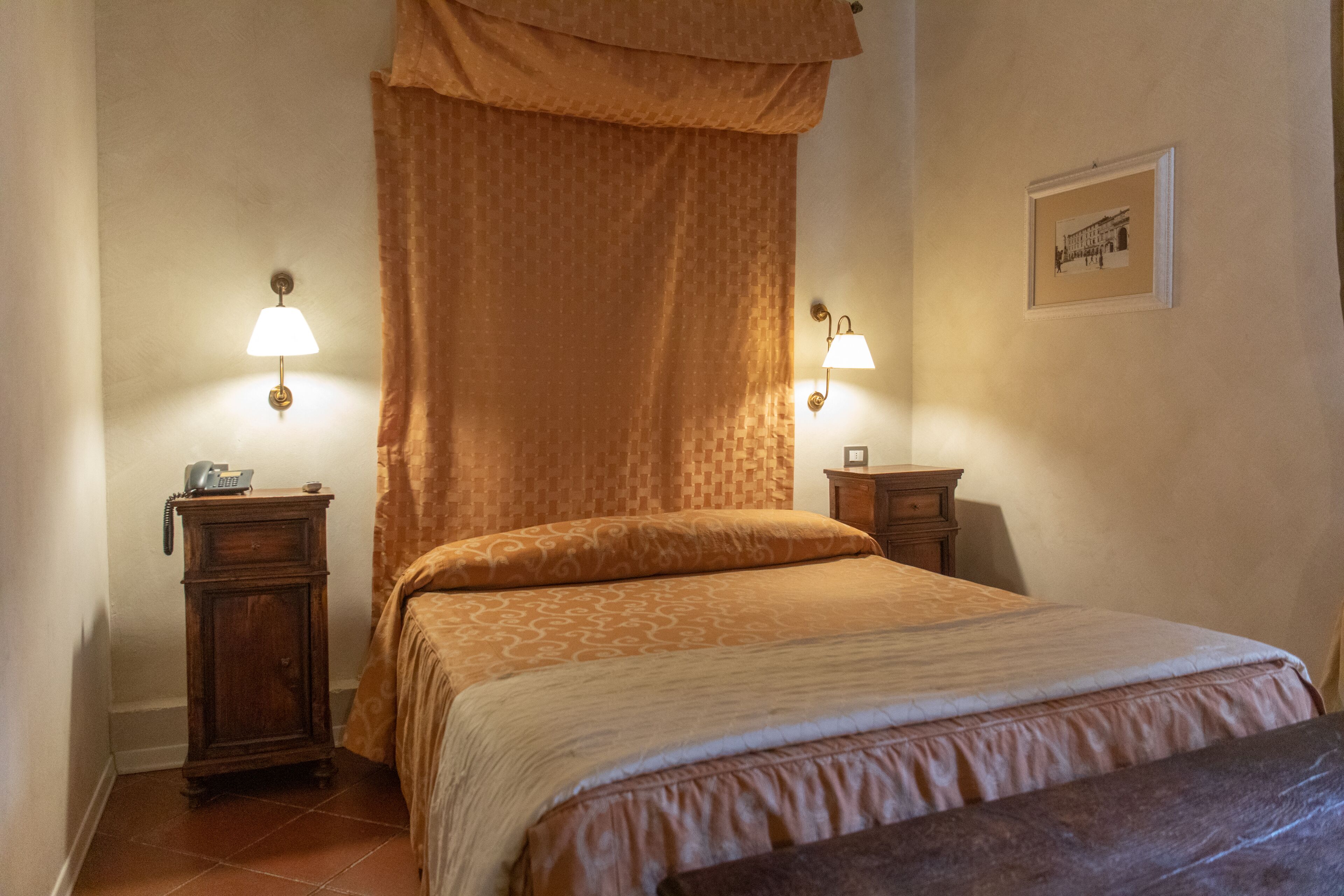 A bedroom with a bed, two bedside tables, a telephone, and a wall-mounted lamp.