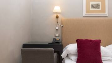 A hotel room with a bed, a desk, a chair, a lamp, a phone, and a framed picture on the wall.