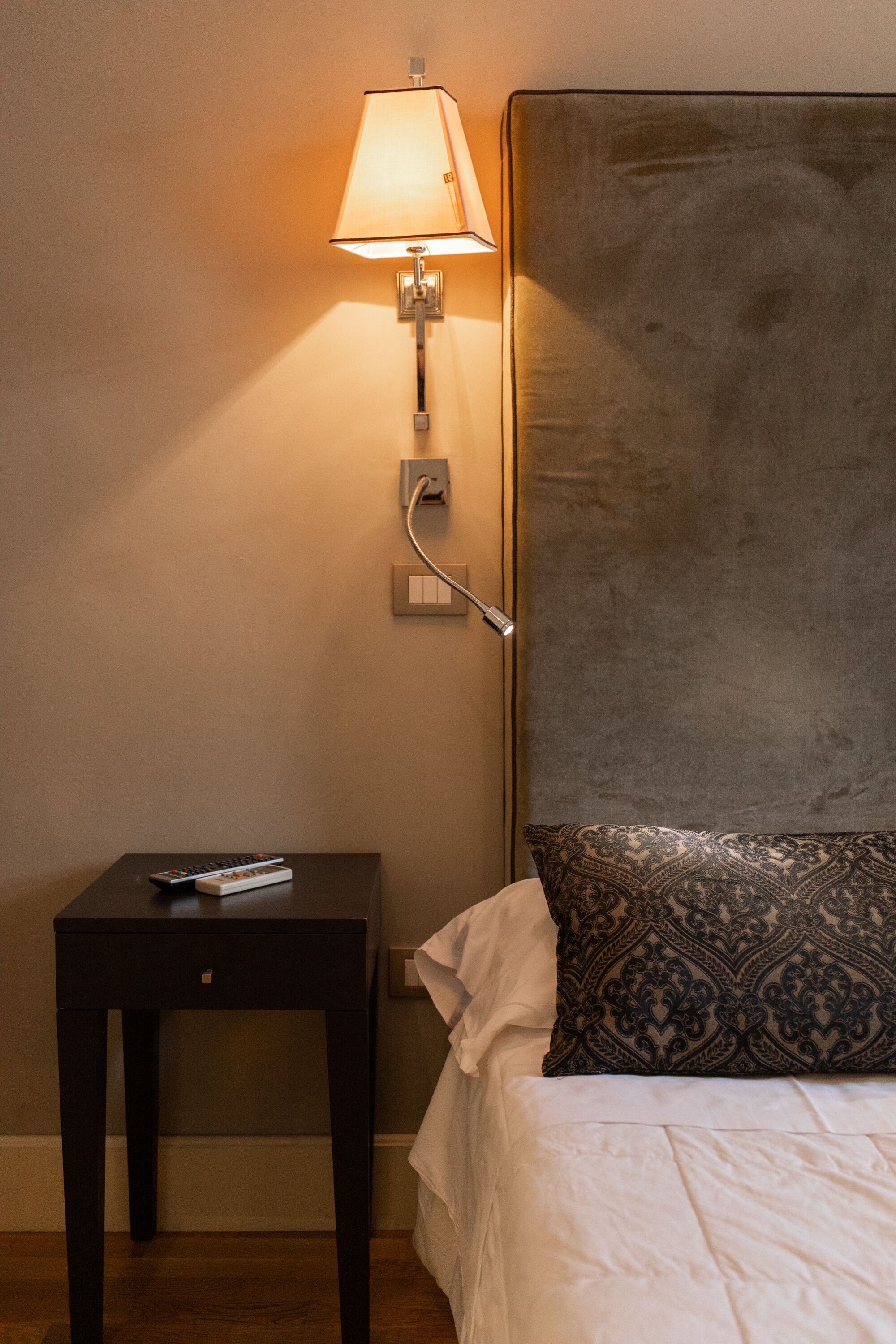 Ein Hotelzimmer mit einem Bett, einem Nachttisch, einer Lampe und einer Steckdose.
