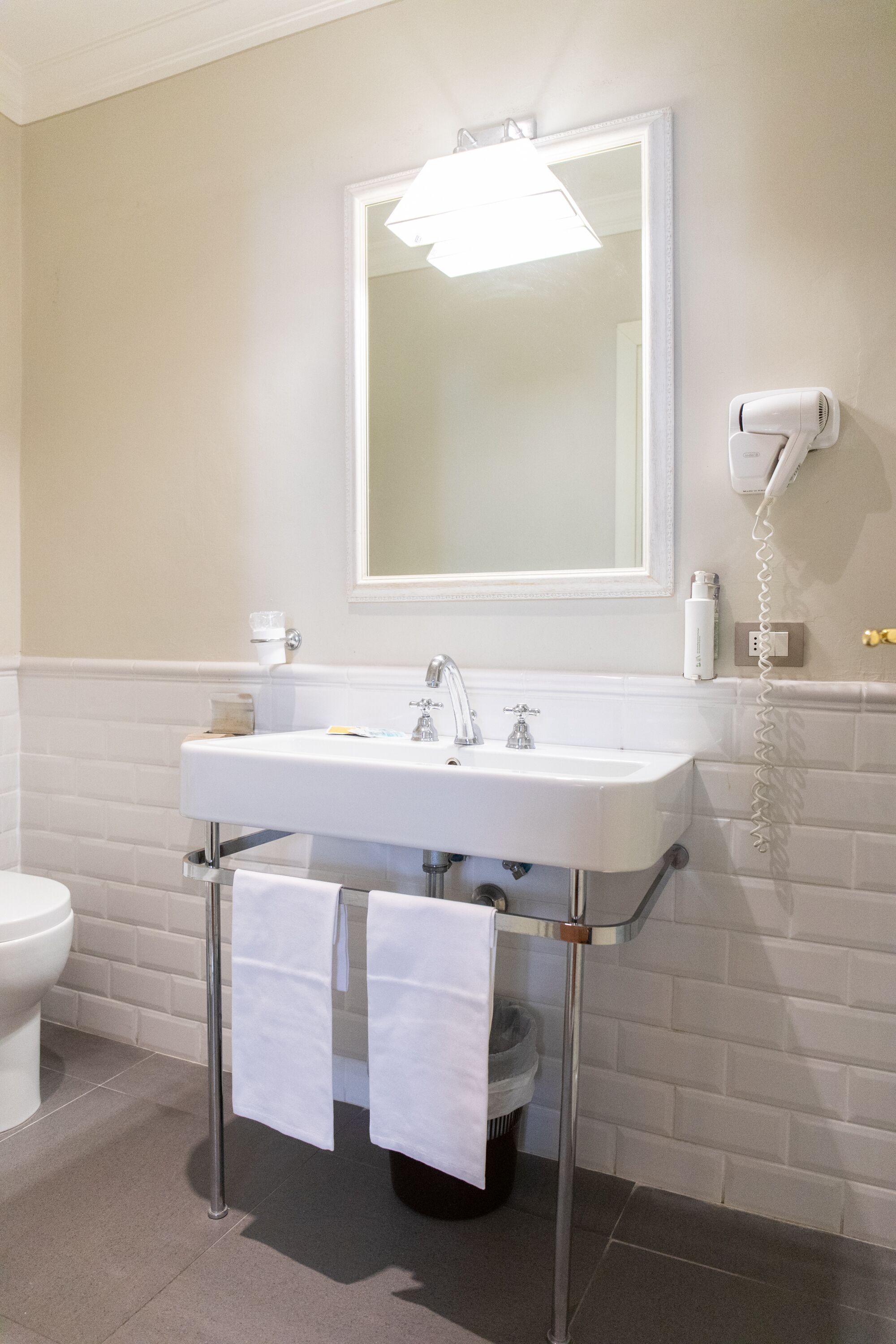 Une salle de bain avec un lavabo blanc, un miroir, un sèche-cheveux et des toilettes.