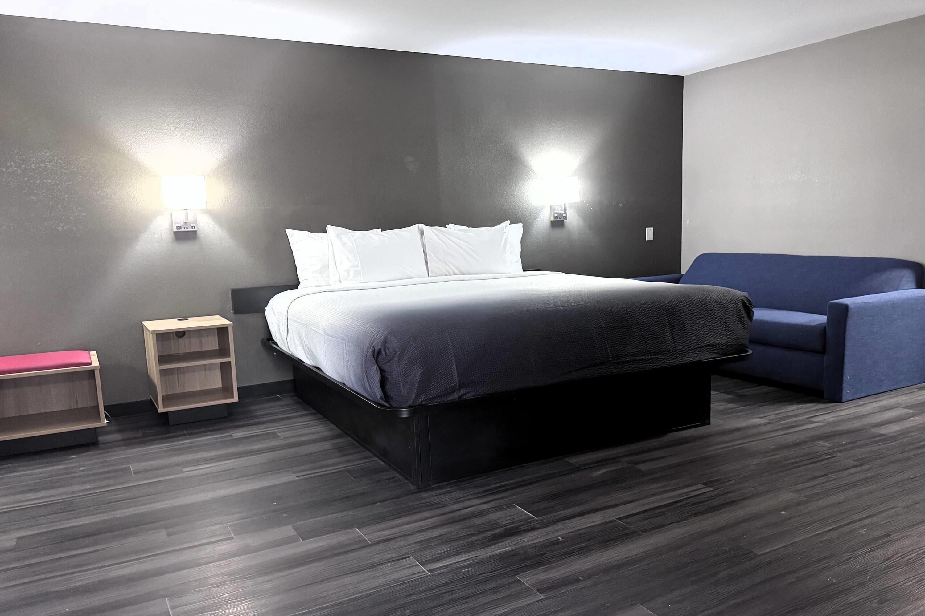 Habitació d'hotel moderna amb un llit gran, taules de nit, zona de seients i il·luminació penjada a la paret.