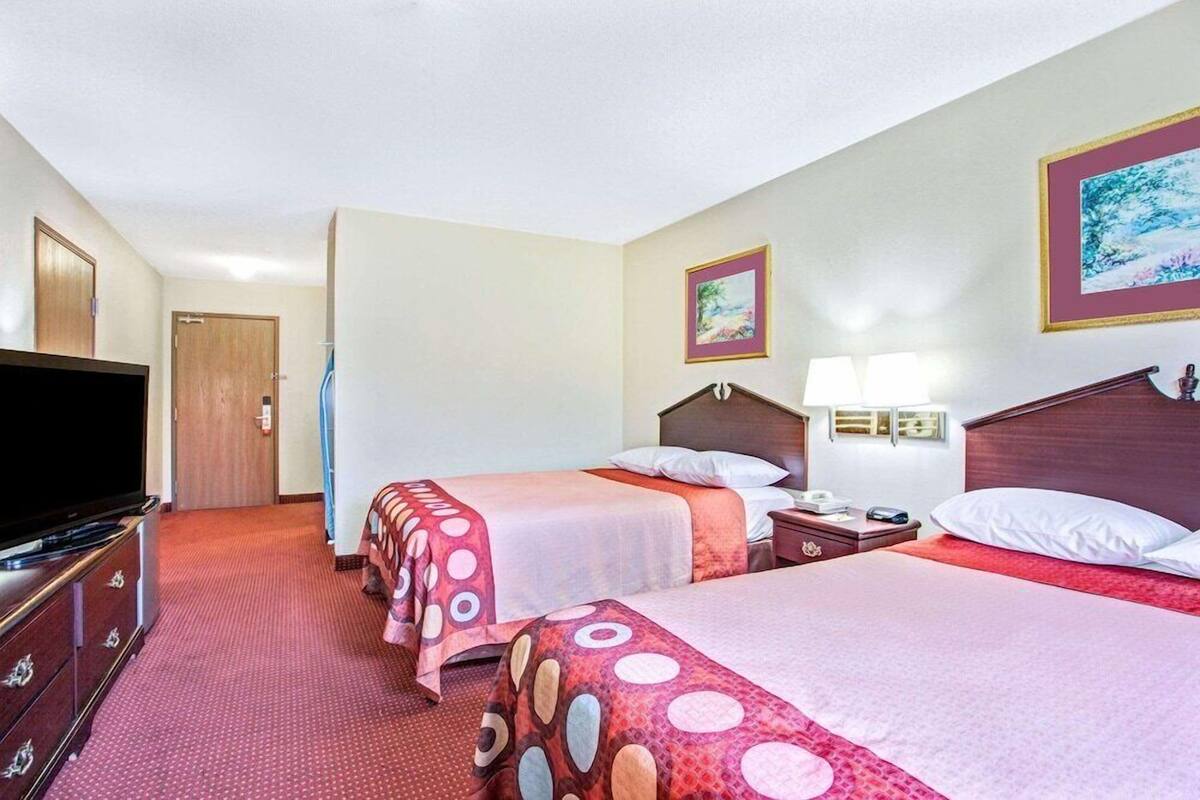 A hotel room with two beds, a TV, a desk, and a lamp.