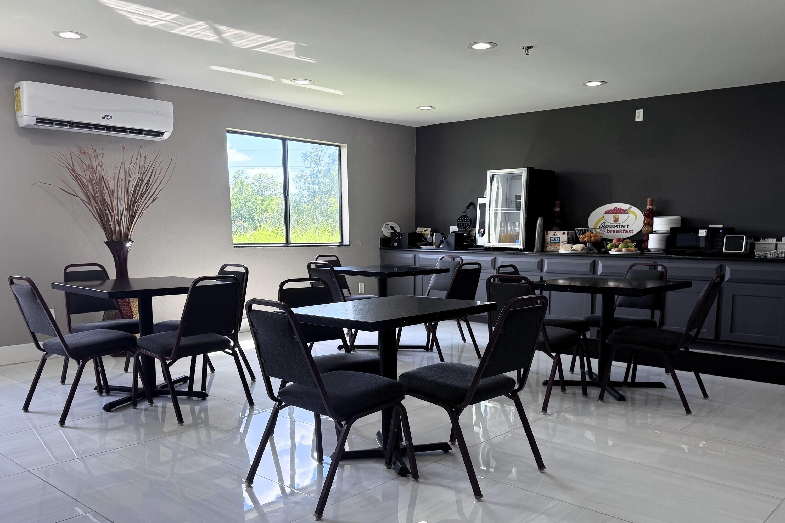 A modern kitchen with a large window, a dining area with black chairs and tables, and a countertop with various appliances.