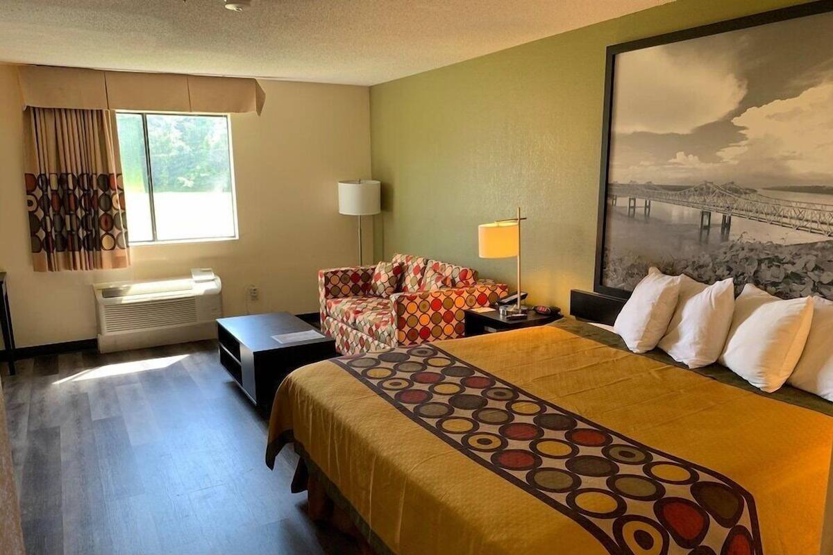 A hotel room with a bed, a sofa, a desk, a lamp, and a large window with curtains.
