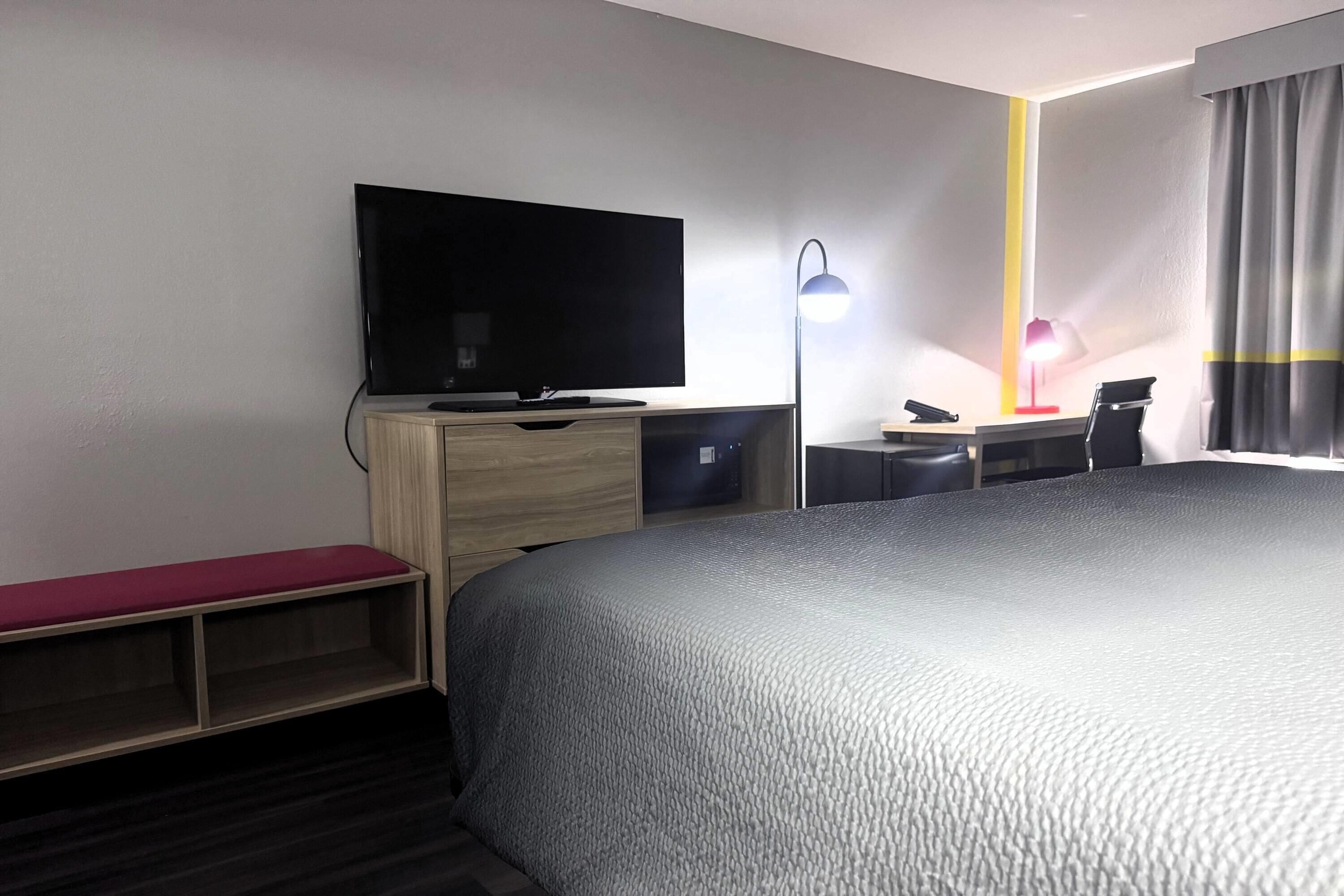 Una camera d'albergo con un letto, una scrivania, una sedia, un televisore e una lampada.