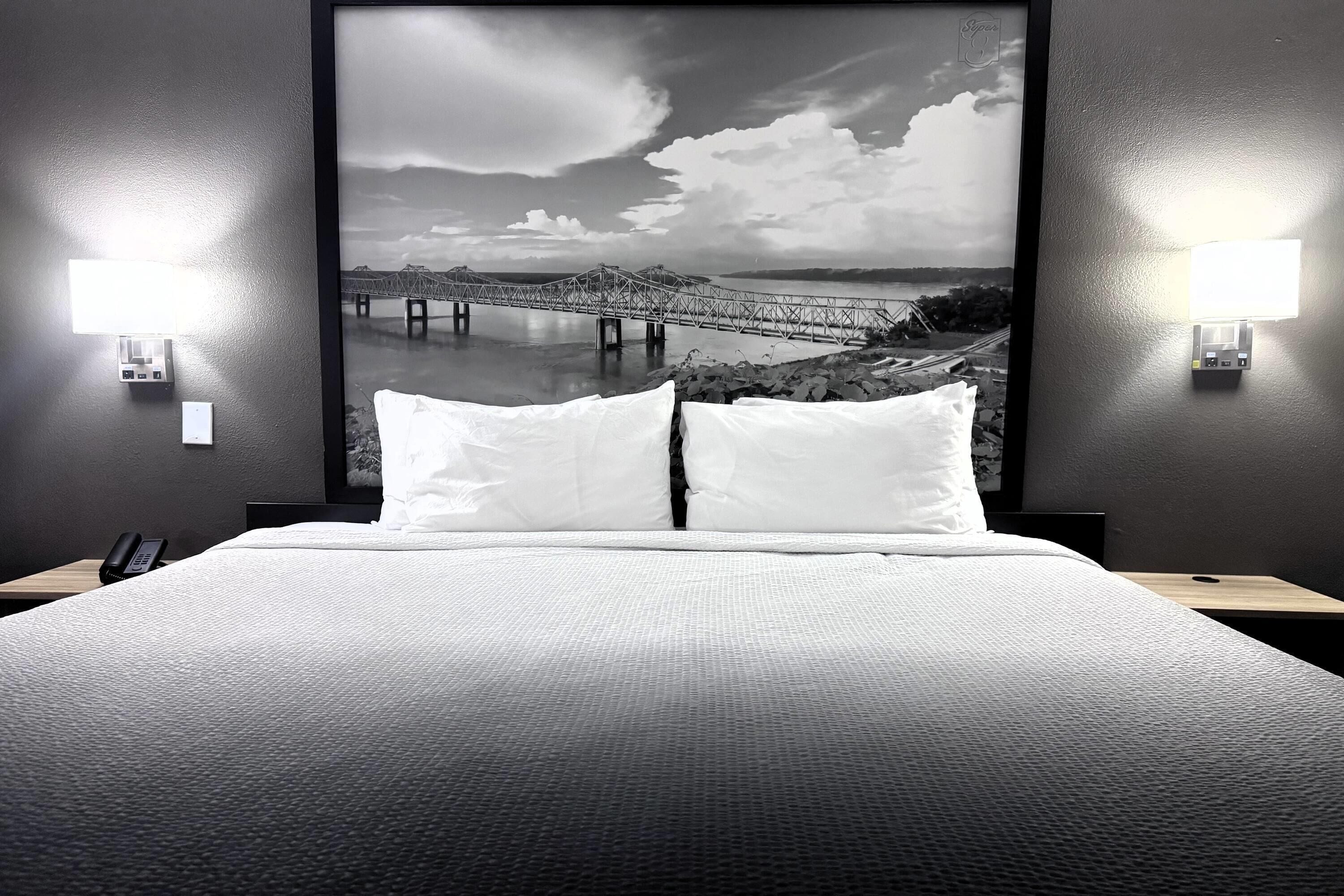 Una habitación de hotel con una cama grande, dos lámparas de noche y un cuadro con una imagen de un puente.