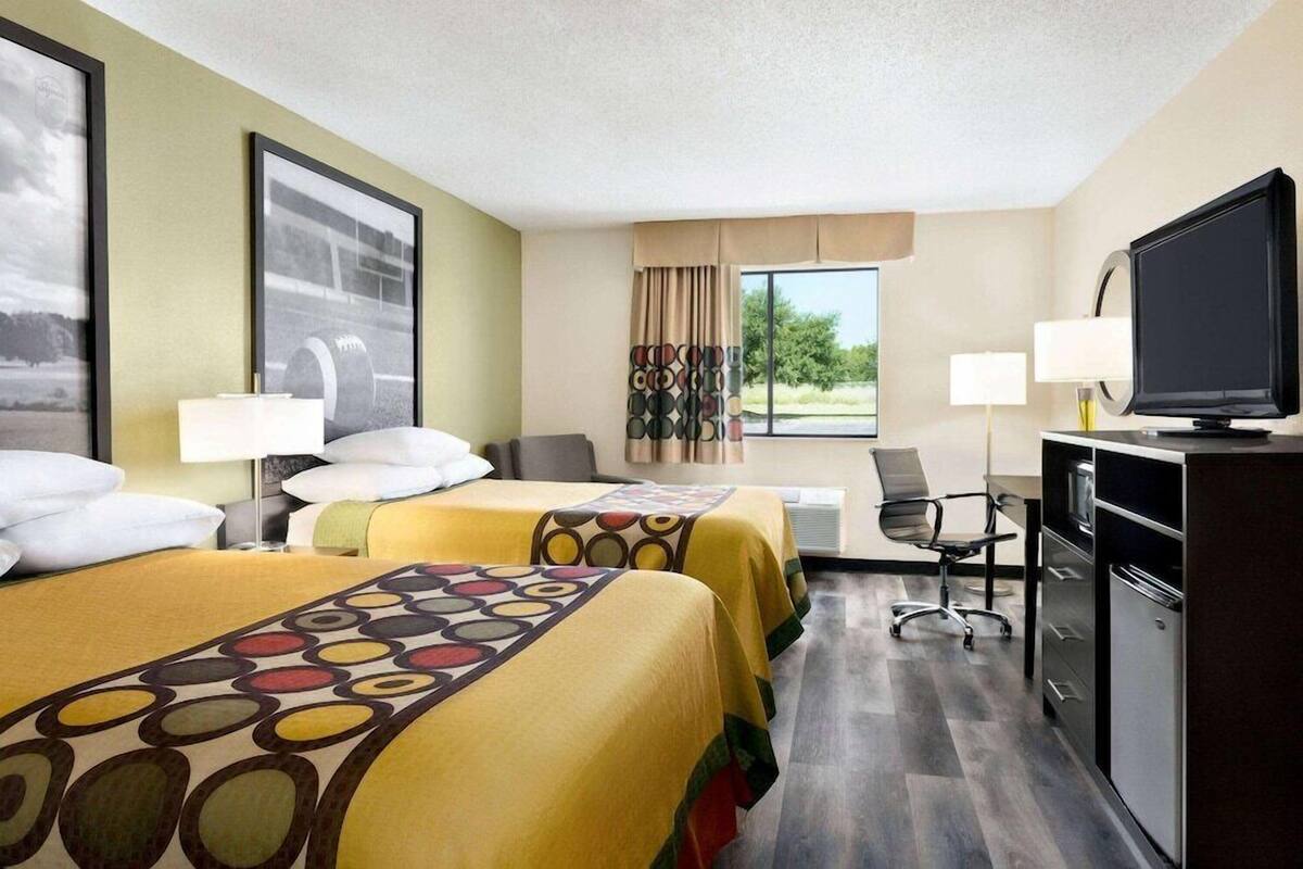 A hotel room with two beds, a desk, a television, and a window with a view of greenery.