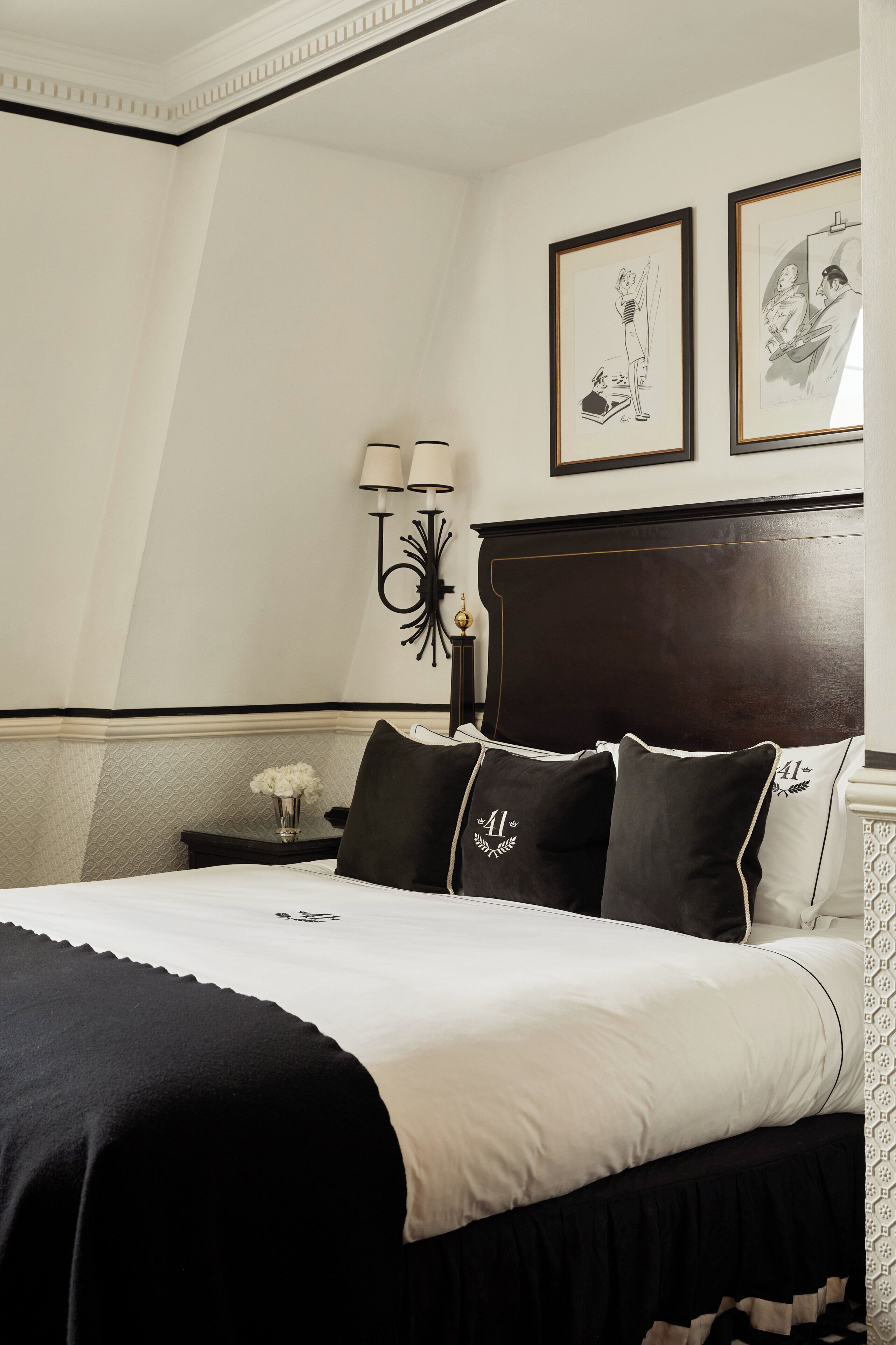 A neatly arranged hotel room with a large bed, a dark wooden headboard, and two framed artworks on the wall.