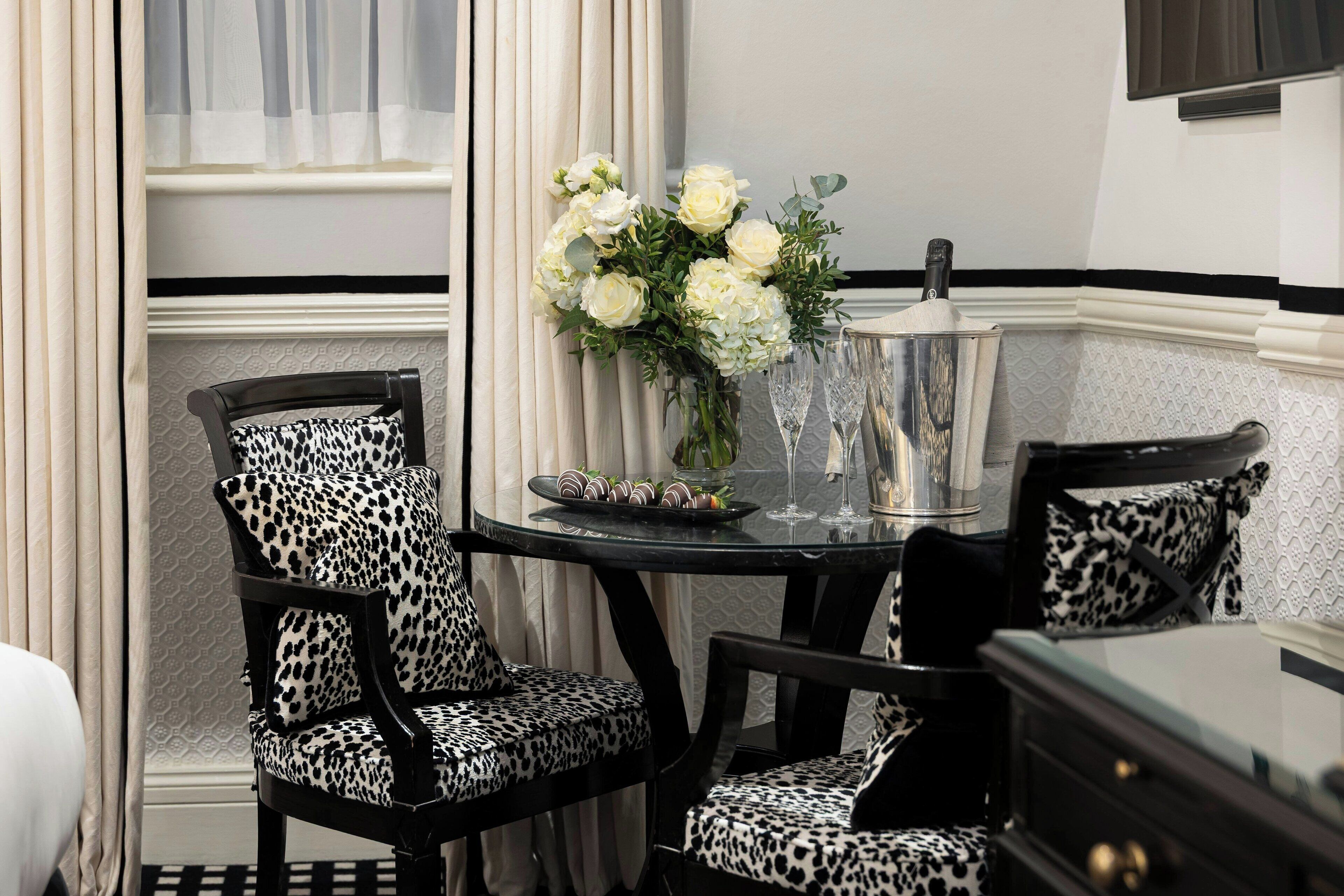 A dining area with a round table, two leopard print chairs, a vase of white flowers, and a tray of chocolates.
