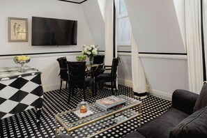 A room with a checkered floor, a dining table with chairs, a TV mounted on the wall, and a sofa.