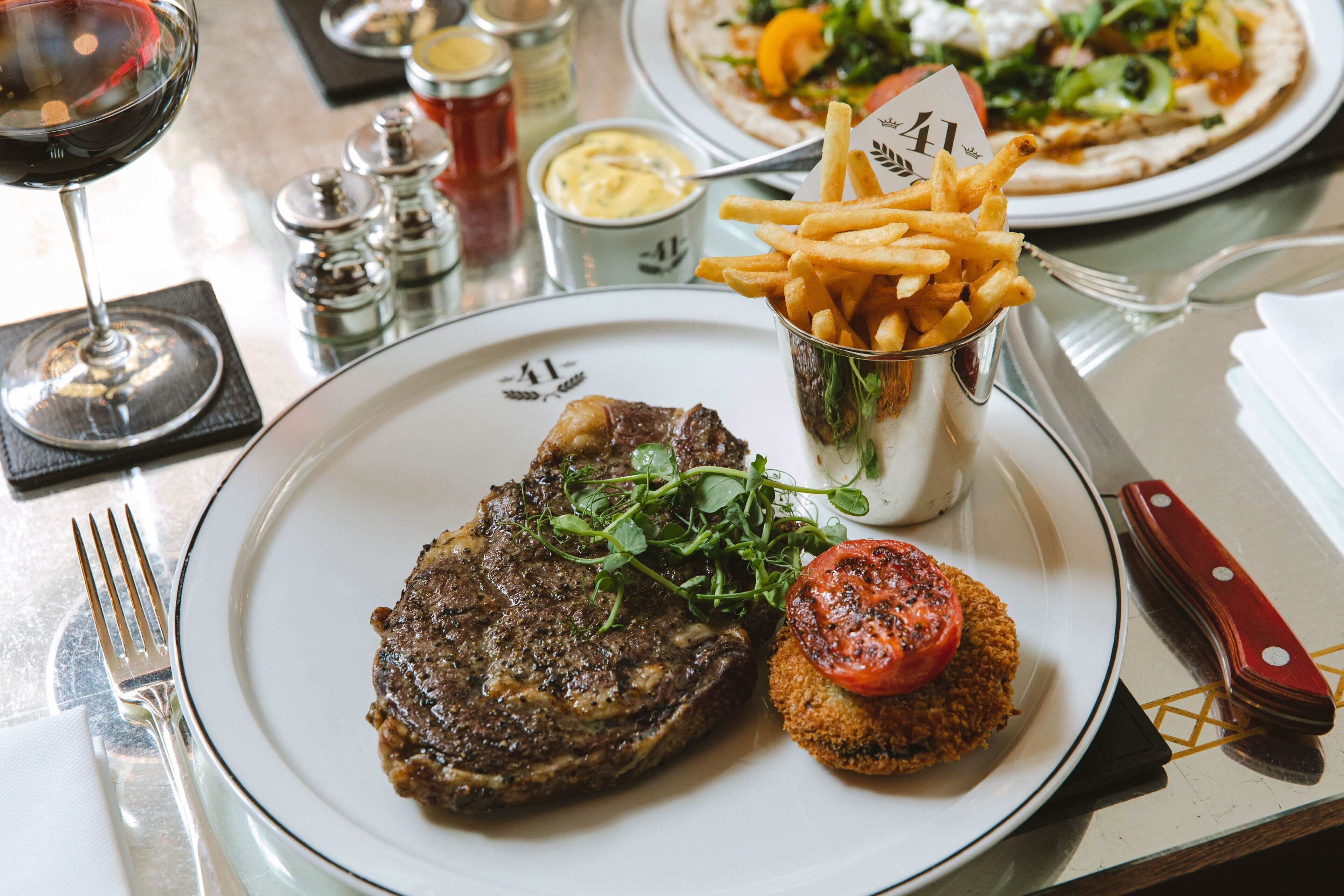 A plate with a steak, fries, and a tomato on a white plate.