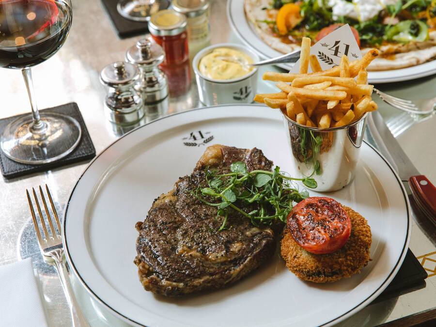 A plate with a steak, fries, and a tomato on a white plate.