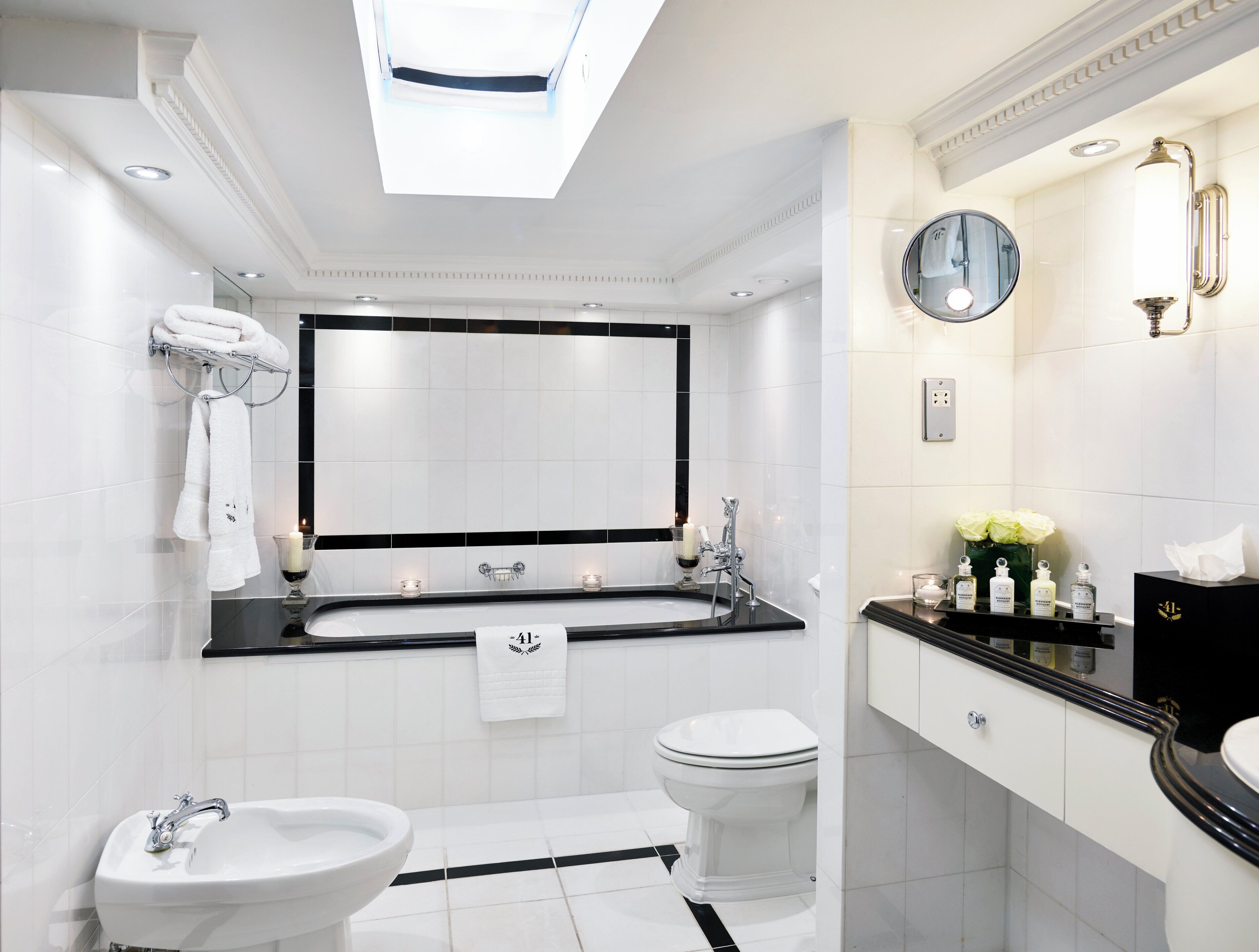 A modern bathroom with a skylight, dual sinks, a toilet, and a vanity with toiletries.