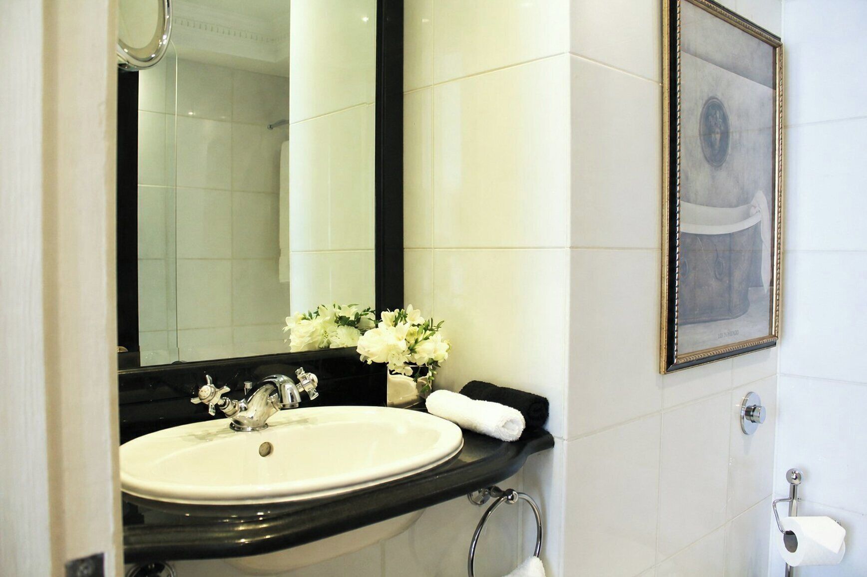 A bathroom with a white sink, a mirror, a framed picture on the wall, and a towel rack.