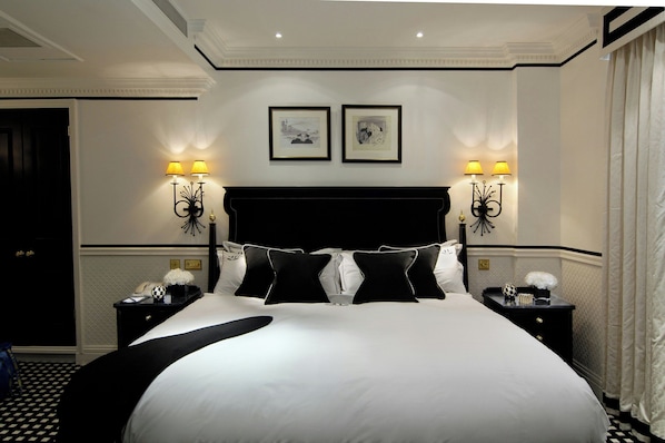 Una habitación de hotel con una cama grande, dos mesitas de noche, un cabecero negro y dos lámparas de pared.