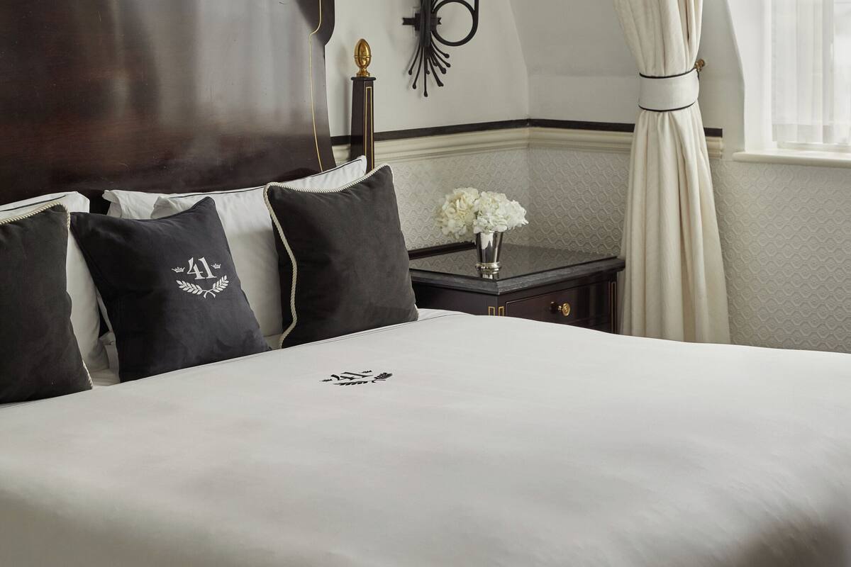 A neatly made bed with dark wood headboard, a bedside table with a lamp, and a window with curtains.