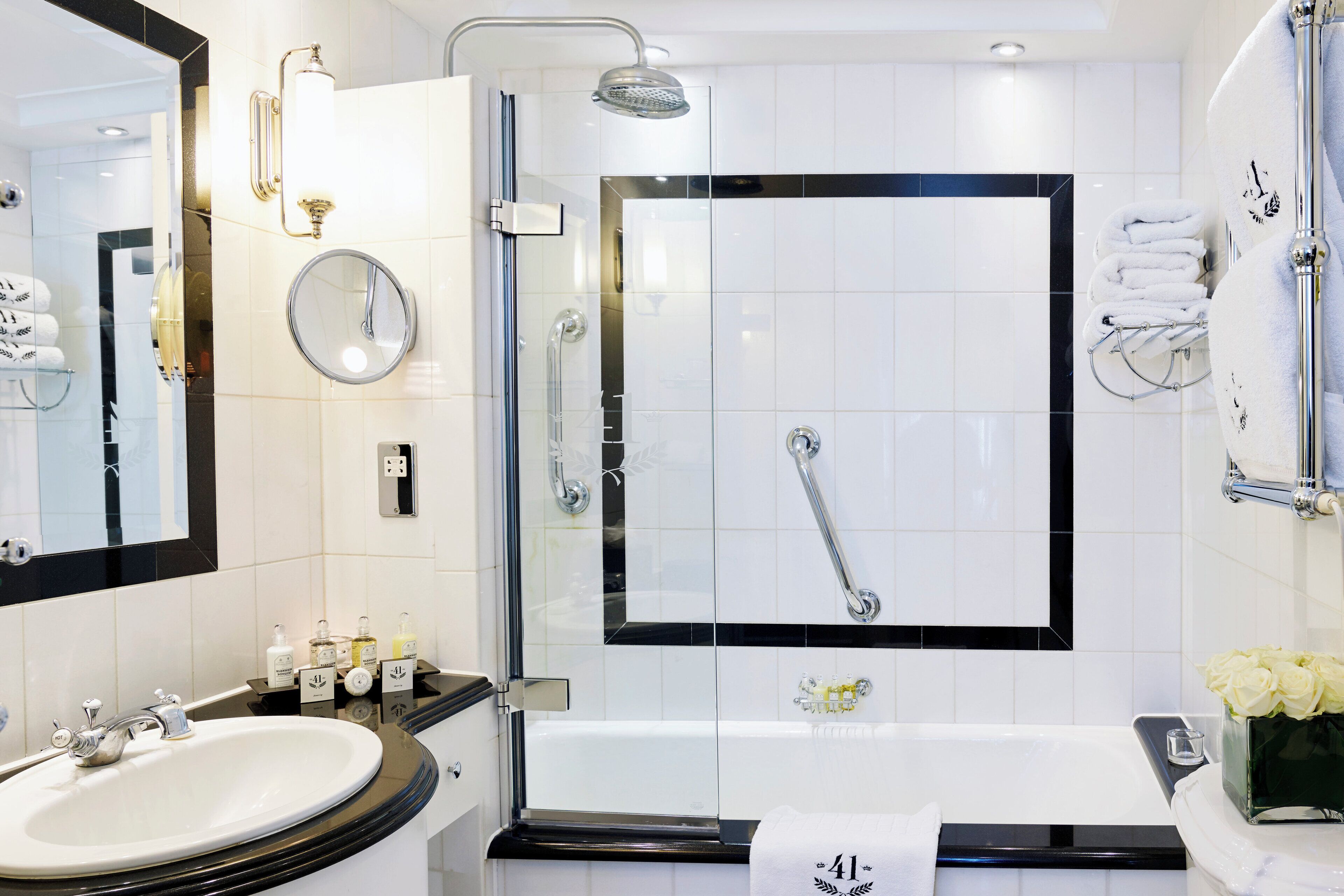 A modern bathroom with a glass-enclosed shower, a white sink, a bathtub, and a vanity with toiletries.