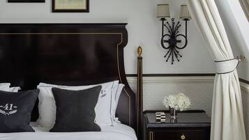 A neatly arranged bedroom with a large bed, a nightstand with a vase of flowers, and two wall-mounted lamps.