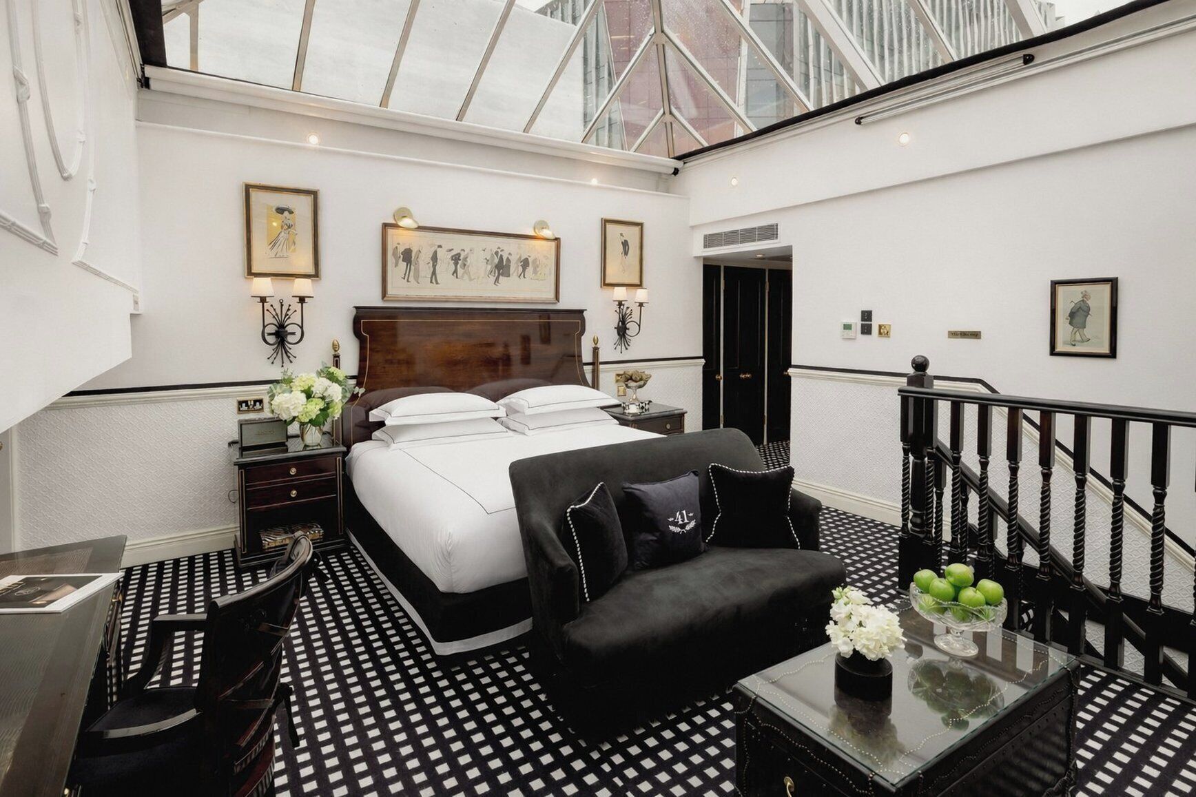 A hotel room with a large bed, a desk, a chair, a small table with a vase, and a staircase.