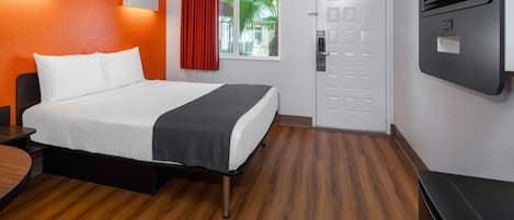 A hotel room with a bed, a desk, a TV, a window with curtains, and a door.