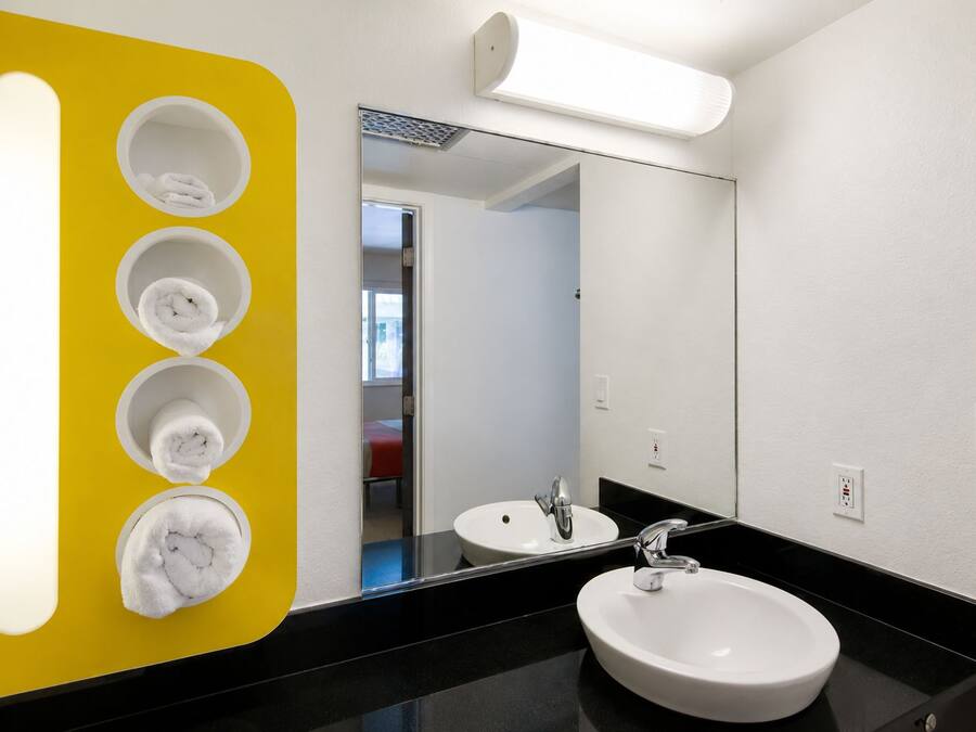 A modern bathroom with a black countertop, a white sink, and a mirror. There are four white towels hanging on a yellow wall.