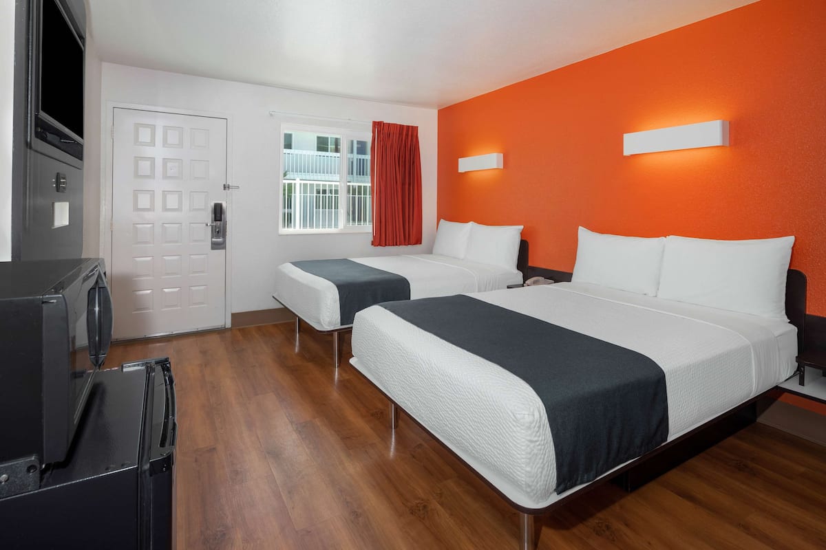 A hotel room with two beds, a TV, and a refrigerator.
