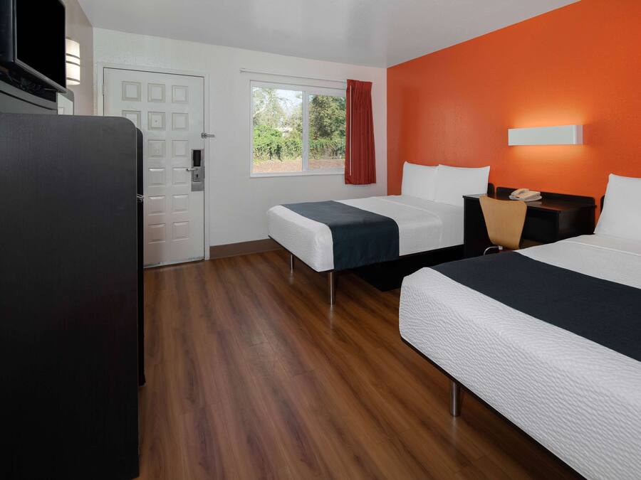 Habitación de hotel con dos camas, un escritorio, una silla, un televisor y una ventana con cortinas.