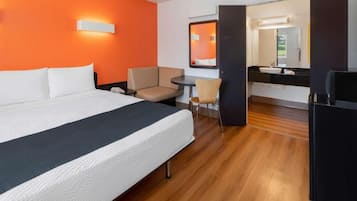 Habitación de hotel con cama, un escritorio pequeño, una silla, un espejo y un refrigerador.