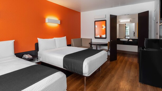 A hotel room with two beds, a desk, a chair, a mirror, and a refrigerator.