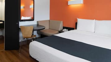 Habitación de hotel con una cama, un escritorio, una silla y una lámpara de pared.
