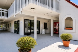 A hotel entrance with a Coca-Cola vending machine, a trash bin, and potted plants. - Vagabond Inn Santa Barbara - Carpinteria South (Carpinteria)