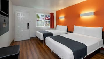 Une chambre d’hôtel avec deux lits, une télévision, une fenêtre avec des rideaux et un mur d’accent de couleur orange.
