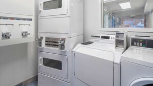 A laundry facility with stacked washing machines and dryers, control panels, and a view of the outside through a window.