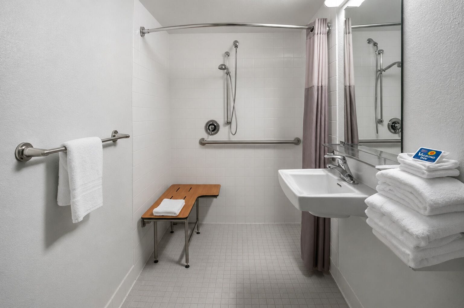 Ein Badezimmer mit Dusche, Waschbecken, Spiegel, Handtuchhalter und einer Sitzbank.