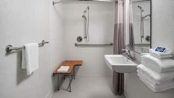 Ein Badezimmer mit Dusche, Waschbecken, Spiegel, Handtuchhalter und einer Sitzbank.