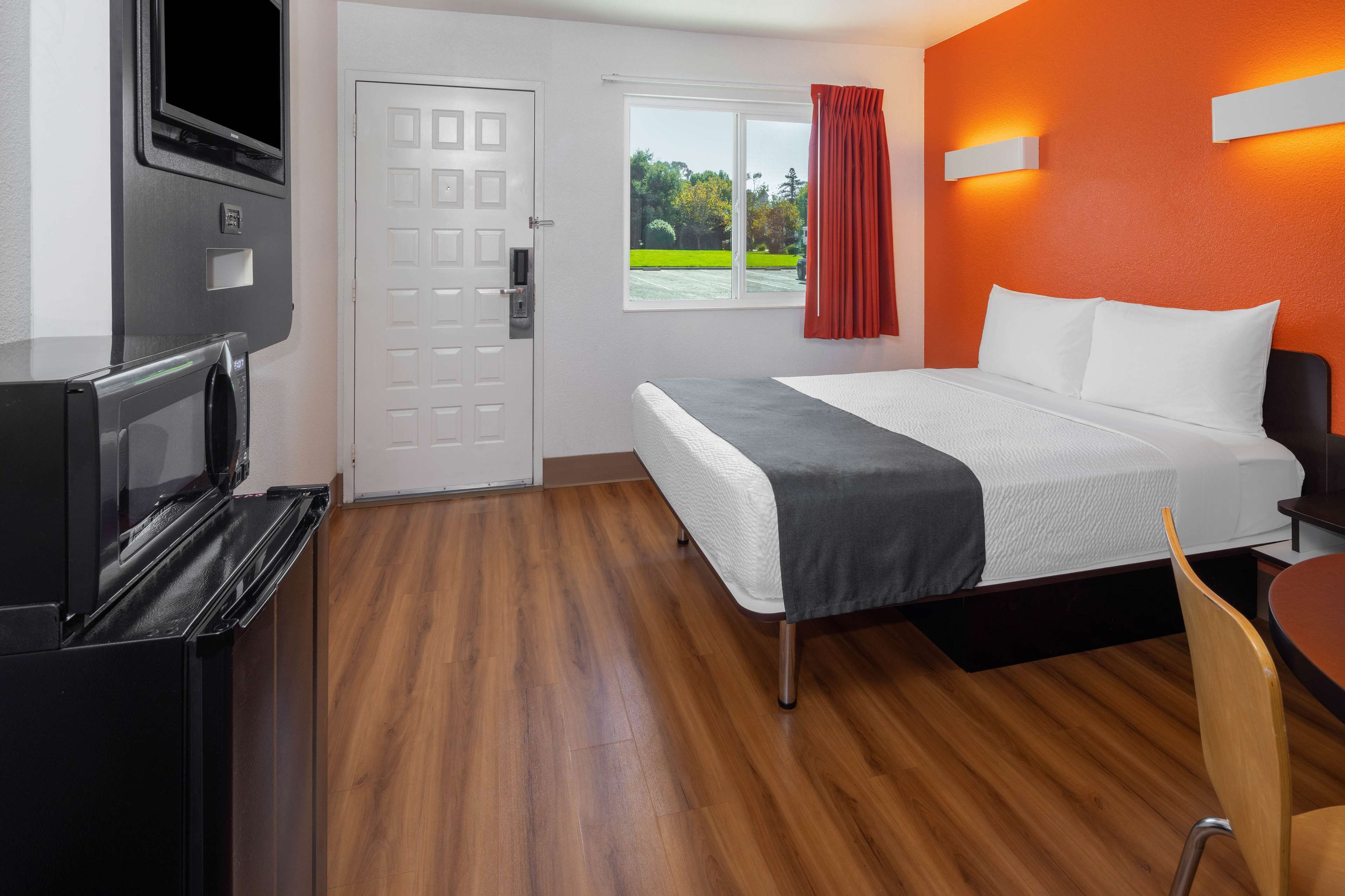 Habitación de hotel con cama, televisión, ventana con cortinas y vista a zonas verdes.