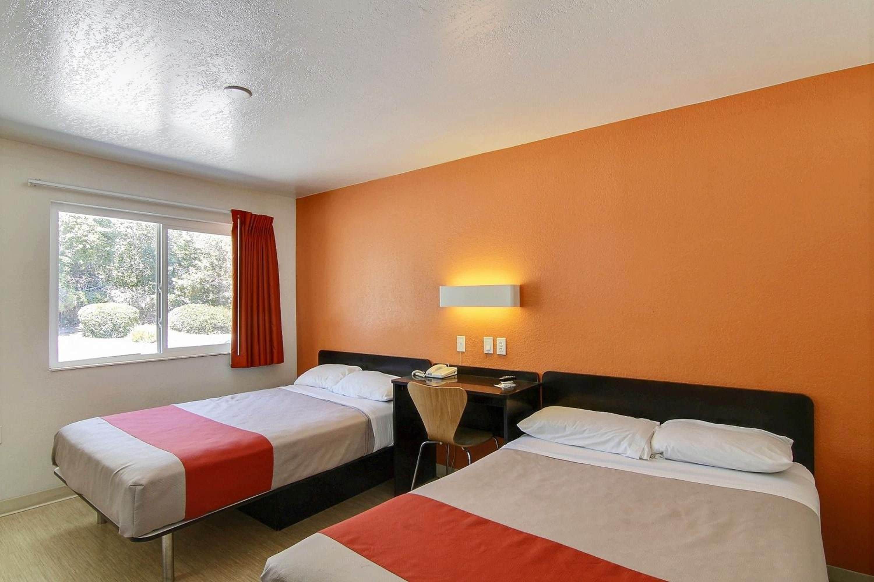 Ein Hotelzimmer mit zwei Betten, einem Vorhangfenster, einem Nachttisch und einer Wandlampe.