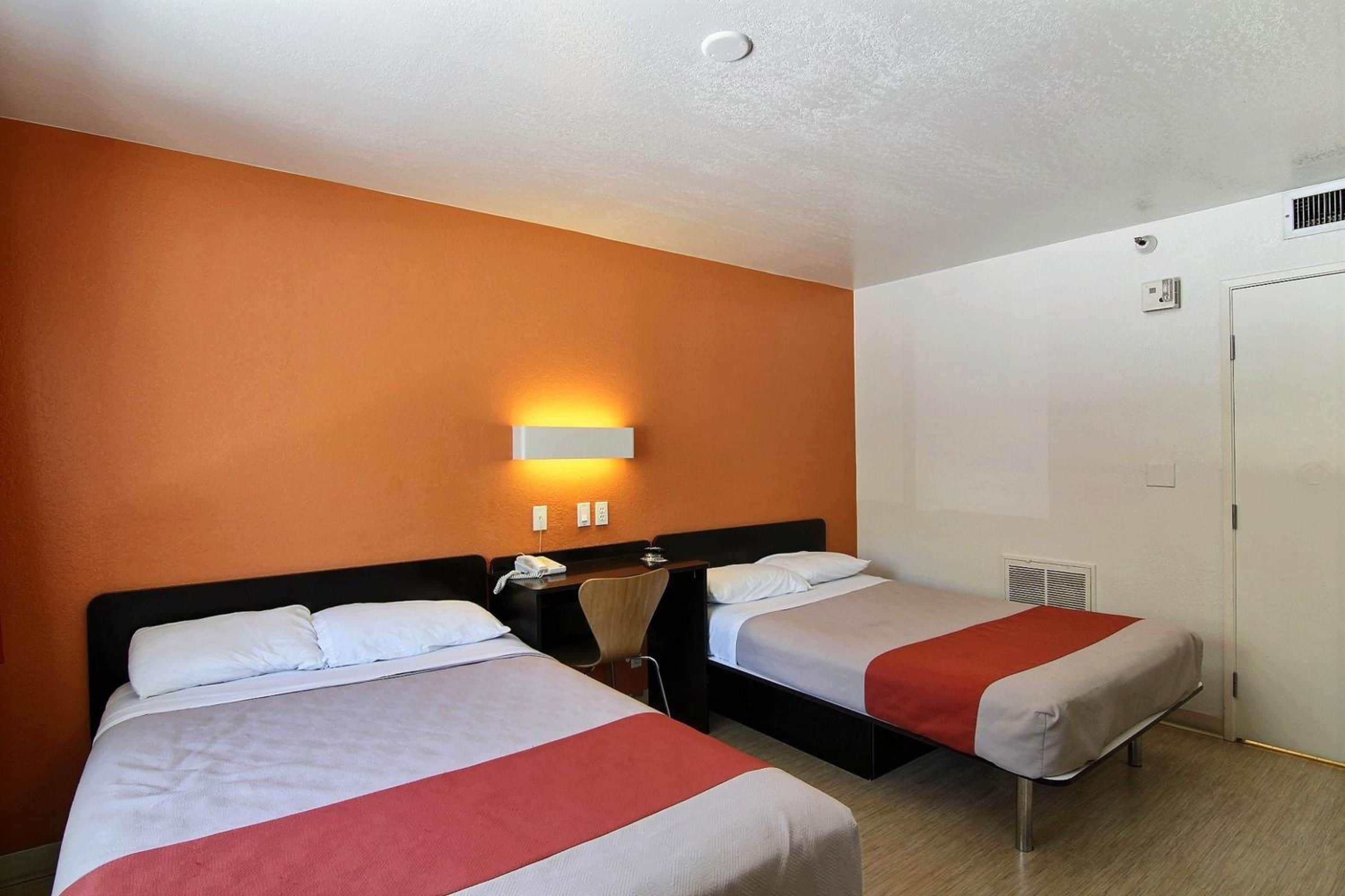 A hotel room with two beds, a desk, a chair, a phone, and a wall-mounted light fixture.
