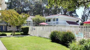 A residential area with a white picket fence, a well-maintained lawn, and a pool area with a red umbrella.