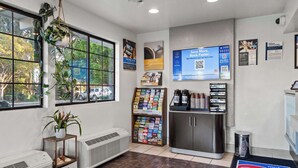 A hotel reception area with a large window, air conditioning units, a display of magazines, and a digital screen advertising a loyalty program.