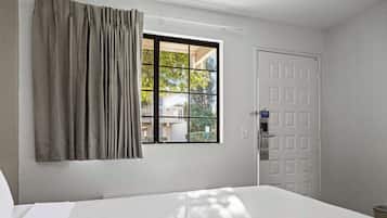 Una habitación de hotel con cama, ventana con cortinas, puerta y vista al exterior.