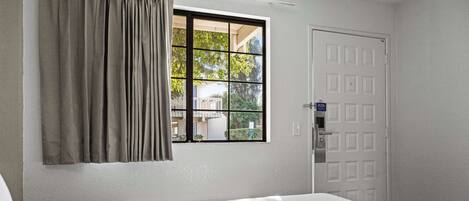A hotel room with a bed, a window with curtains, a door, and a view of the outside.