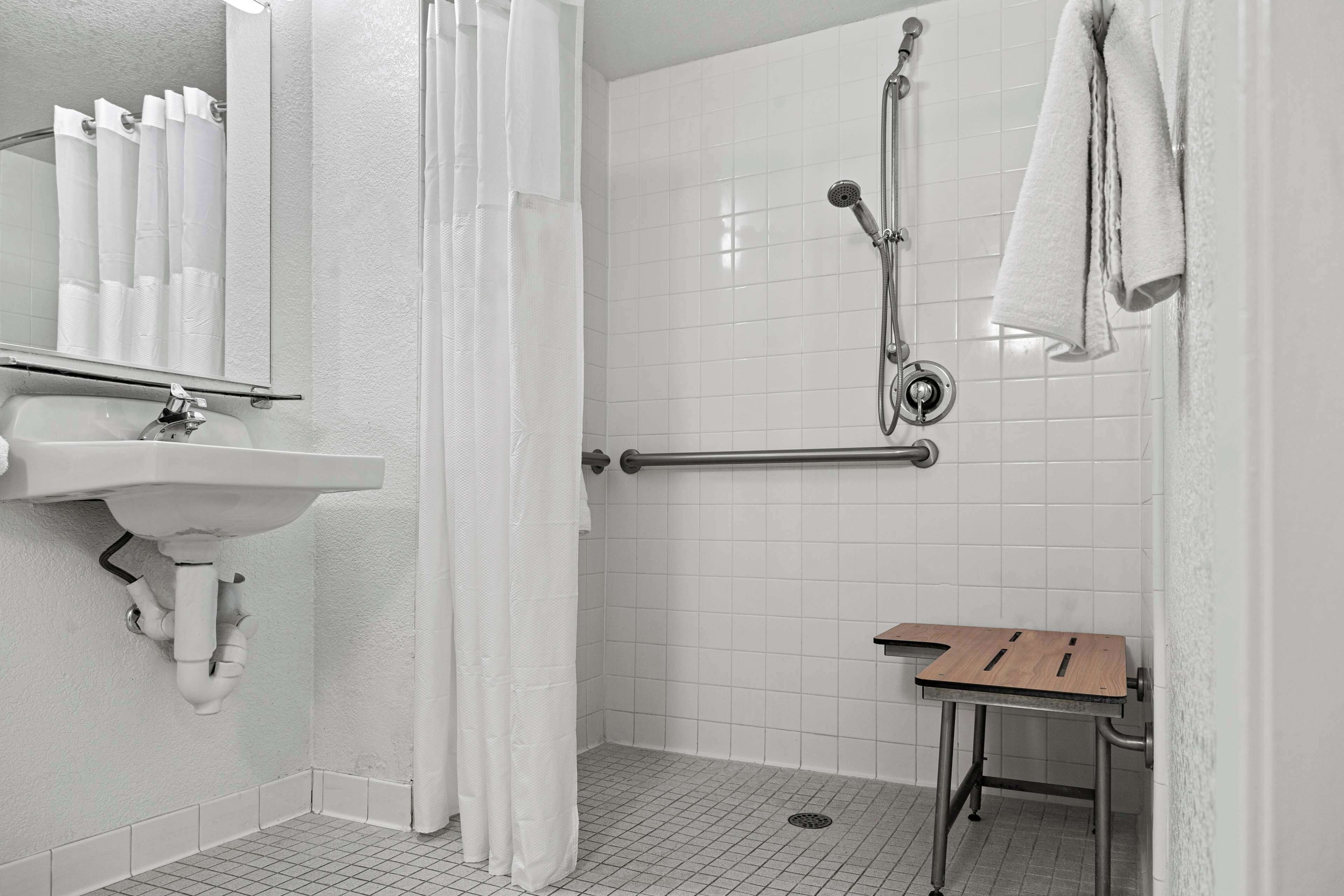 Un baño moderno con un lavamanos blanco, ducha con barra de apoyo y tocador de madera.