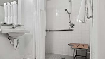 Un baño moderno con un lavamanos blanco, ducha con barra de apoyo y tocador de madera.